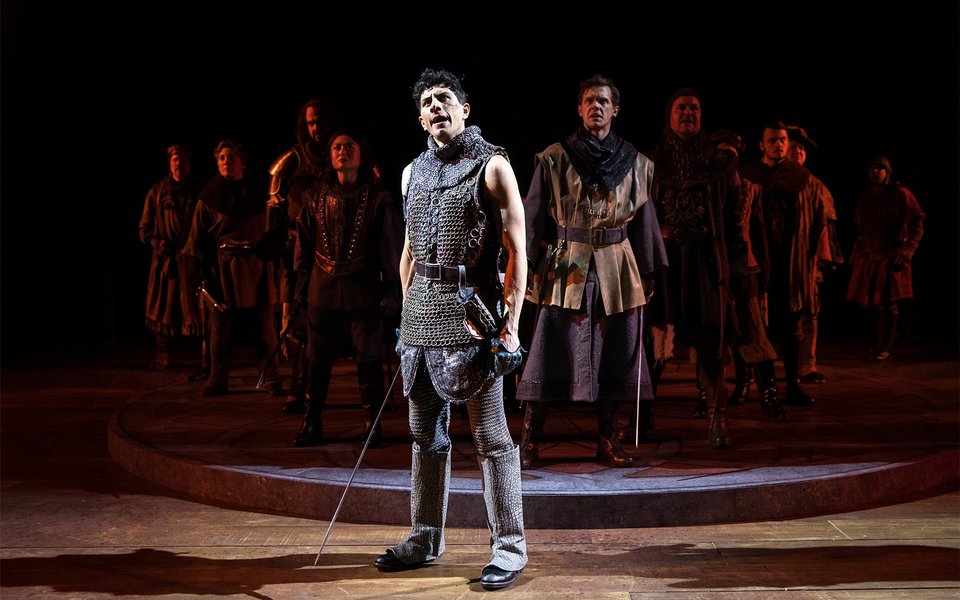 Daniel Molina stands center stage, the company behind him, during a scene from Henry V.