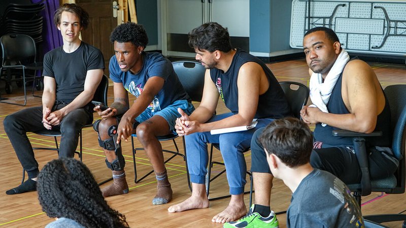 A group of adult students sit in black chairs listening intently during a Guthrie Workshop